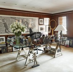 a glass table topped with lots of assorted items in front of a wall mounted art piece