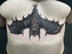 a woman's back with a bat tattoo on her chest and the bottom part of her stomach