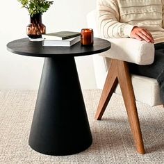 a man sitting in a chair next to a table with a book and vase on it