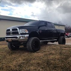 a large black truck parked on top of a grass covered field next to a building