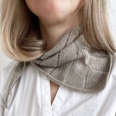 a woman with blonde hair wearing a white shirt and gray knitted cowl neck scarf