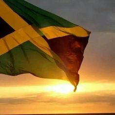 the sun is setting behind a large green and yellow flag in front of an ocean