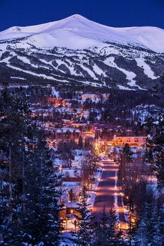 a snowy mountain is in the background with houses and trees on it at night time