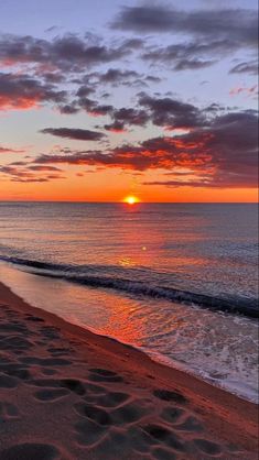 the sun is setting over the ocean with clouds in the sky and sand on the beach