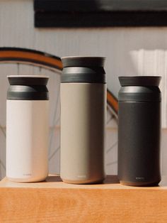 three insulated coffee cups sitting on top of a wooden table next to a bicycle