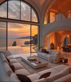 a living room filled with white furniture and large windows overlooking the ocean at sunset or dawn