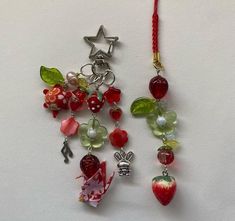 two necklaces with charms hanging from them on a white surface, one has an apple and the other is a strawberry