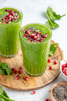 two green smoothies with pomegranates in them on a wooden tray