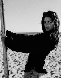 black and white photograph of a woman leaning on a pole at the beach with her arms crossed