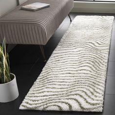 a white rug on the floor next to a bench and potted plant in front of a window