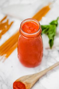 a jar filled with red sauce sitting on top of a white counter next to some vegetables