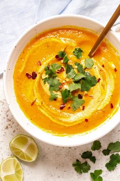 a white bowl filled with soup and garnished with cilantro, parsley and lime