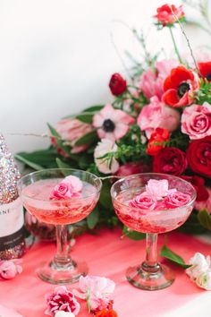 two glasses filled with pink liquid next to a bottle of wine and flowers on a table