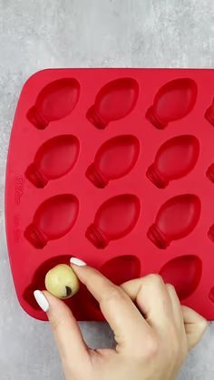 a woman is placing an olive into a red ice tray that has holes in it