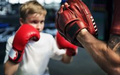 a young boy wearing boxing gloves standing next to an adult