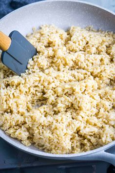 rice being cooked in a skillet with a spatula on the side and wooden spoon