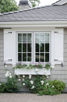 a window with white shutters and flowers on the windowsill in front of a house