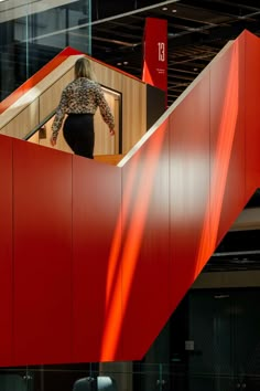 a woman is walking up the stairs in an office building with red walls and glass windows