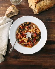 a white bowl filled with soup next to bread on top of a wooden table,