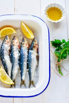 three fish in a bowl with lemon slices and parsley on the side next to it