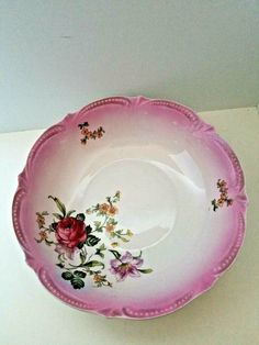 a pink and white plate with flowers on it sitting on top of a table next to a wall