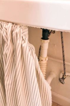 the curtain is pulled back to reveal an exposed pipe in the bathtub and under the sink