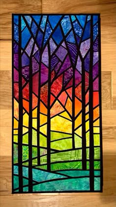 a colorful stained glass window with trees in the middle and mountains behind it on a wooden wall