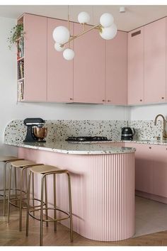 a kitchen with pink cabinets and gold stools in front of an island countertop