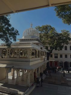 a white building with a dome on top in the middle of a courtyard surrounded by trees