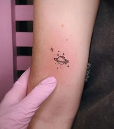 a small saturn tattoo on the left inner arm, with stars and planets around it