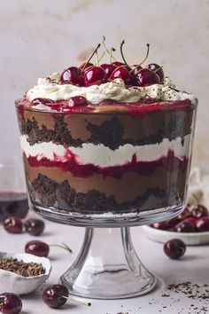 a cake with cherries and whipped cream on top is sitting on a glass pedestal