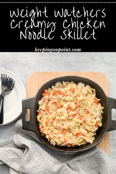 a skillet with noodles and carrots in it on a cutting board next to a plate