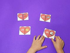 someone is making matching cards with their hands on a purple surface, which includes hearts and the letter h