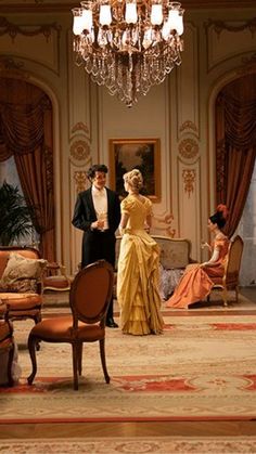 a man and woman in formal dress standing next to each other near a chandelier