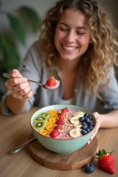 a woman eating a bowl of fruit with a spoon