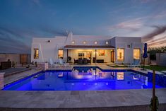 a house with a swimming pool in front of it at night, lit up by blue lights