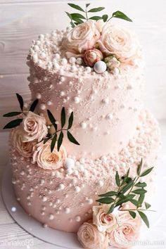 a three tiered wedding cake with pink flowers on top and greenery around the edges