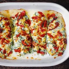 a white casserole dish filled with cheese and tomatoes covered in spinach leaves