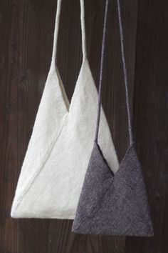 two bags hanging from hooks on a wooden wall, one is white and the other is grey