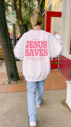 a woman is walking down the sidewalk with a jesus saves sweatshirt on her back,