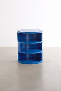 a blue table sitting on top of a cement floor next to a white wall with two shelves