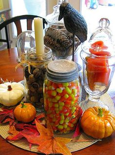 a table topped with jars filled with candy and pumpkins on top of a wooden table