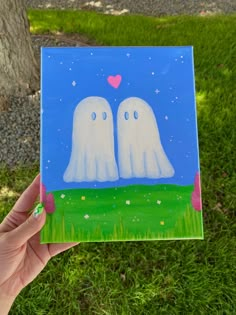 someone is holding up a card with two ghost faces in front of a tree and grass field