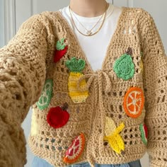 a woman wearing a crocheted sweater with fruit and vegetables on it, standing in front of a door