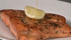 a piece of salmon on a white plate with a lemon wedge sticking out of it