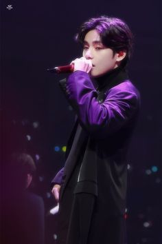 a male in a black suit and purple shirt is holding a microphone to his mouth