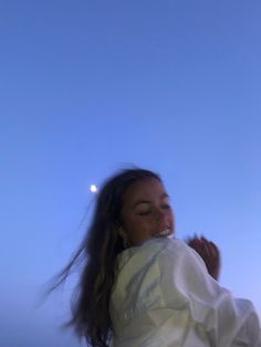 a woman in white shirt flying a kite on the beach at night with full moon behind her