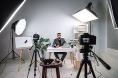 a man sitting at a table in front of a camera and lighting equipment on a tripod