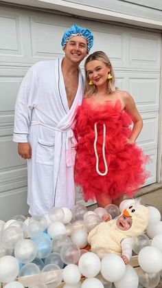 a man and woman dressed in costumes standing next to a baby on a bed of balloons