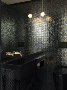 a bathroom with black and gold mosaic tiles on the wall, sink and toilet area